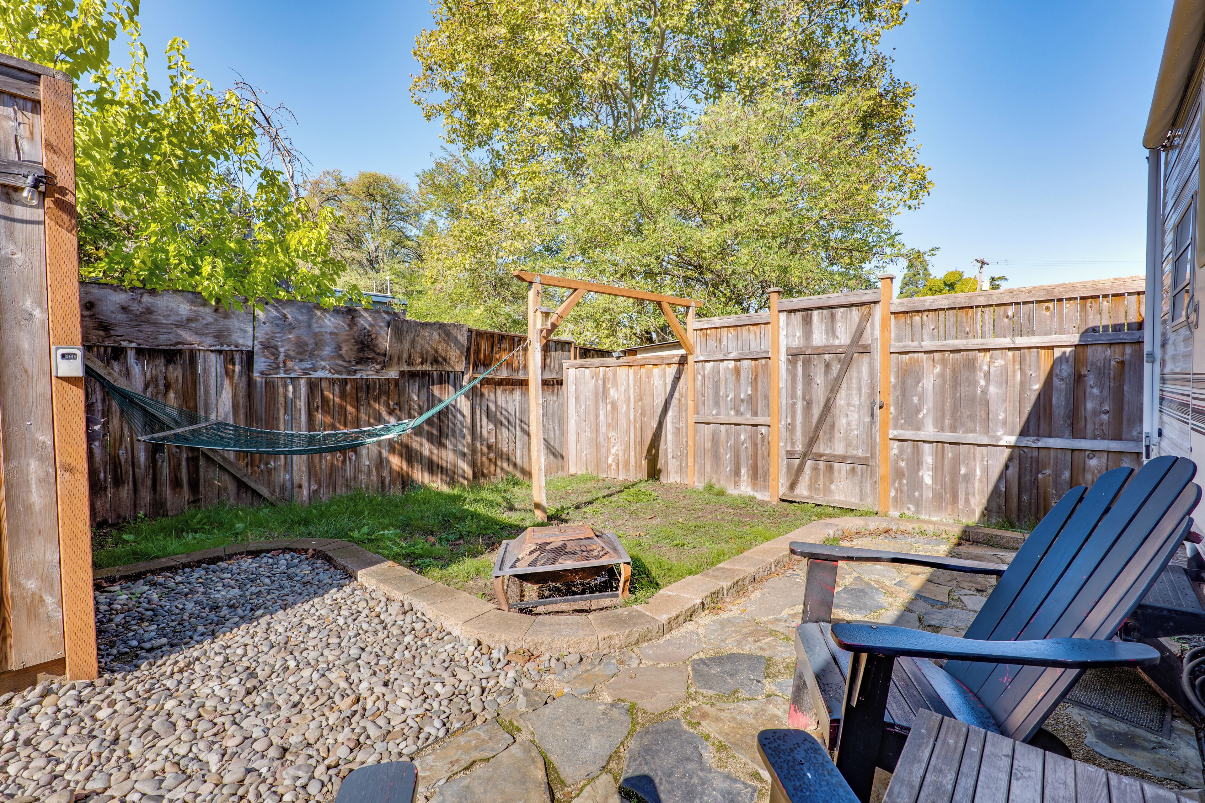 Un jardin avec une clôture en bois, un hamac, un foyer et un espace patio aménagé avec des fauteuils Adirondack.
