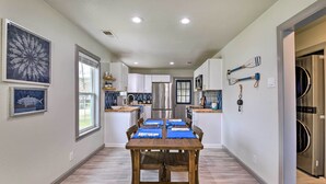 A modern kitchen with white cabinets, stainless steel appliances, and a wooden dining table with blue placemats. - Lake Granbury Getaway ~ 1 Block to Waterfront (Granbury)