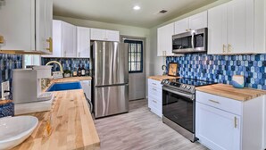 A modern kitchen with white cabinets, stainless steel appliances, a wooden countertop, and a blue-tiled backsplash. - Lake Granbury Getaway ~ 1 Block to Waterfront (Granbury)