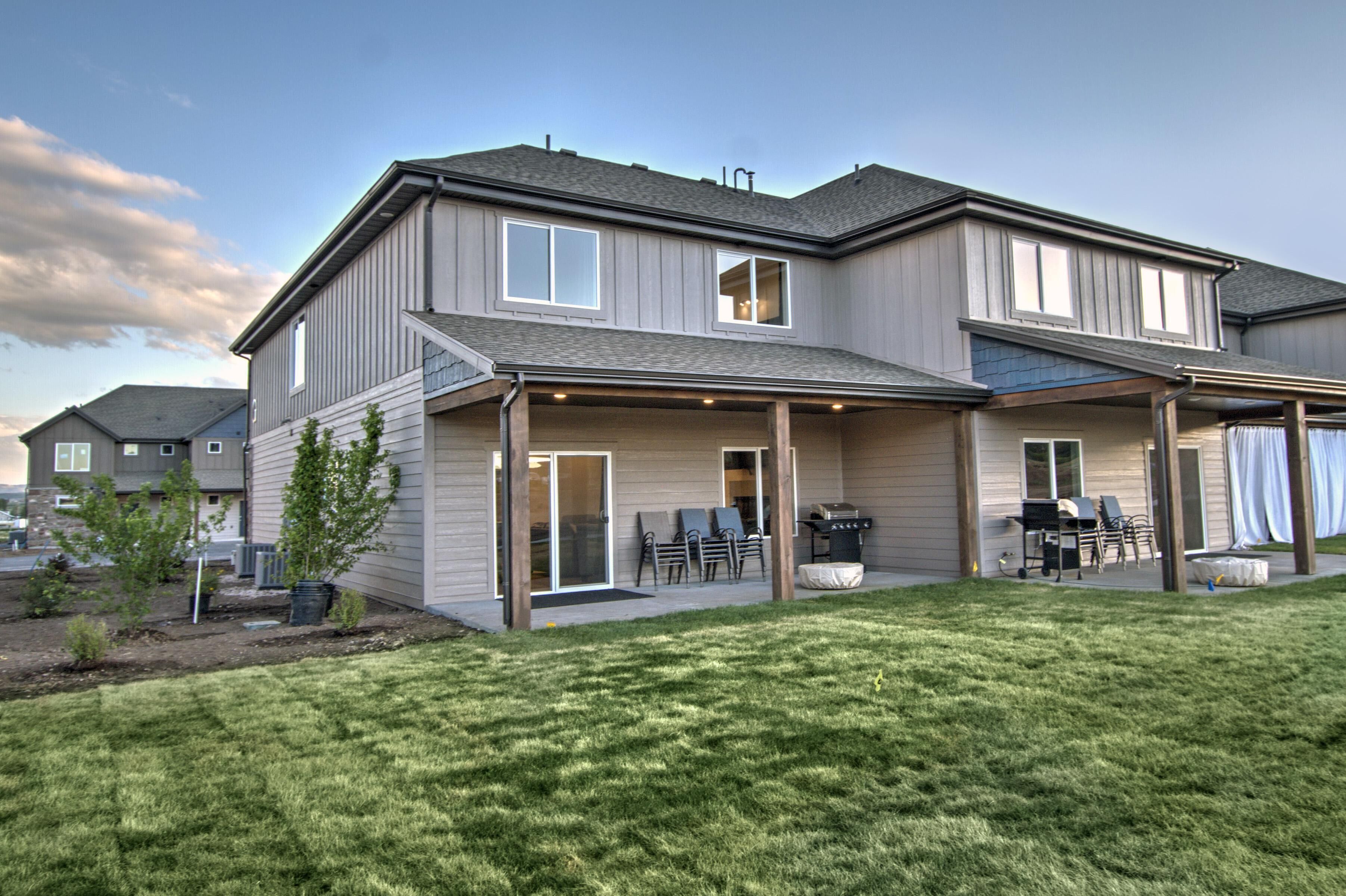 A two-story house with a covered patio, a barbecue area, and a small garden.