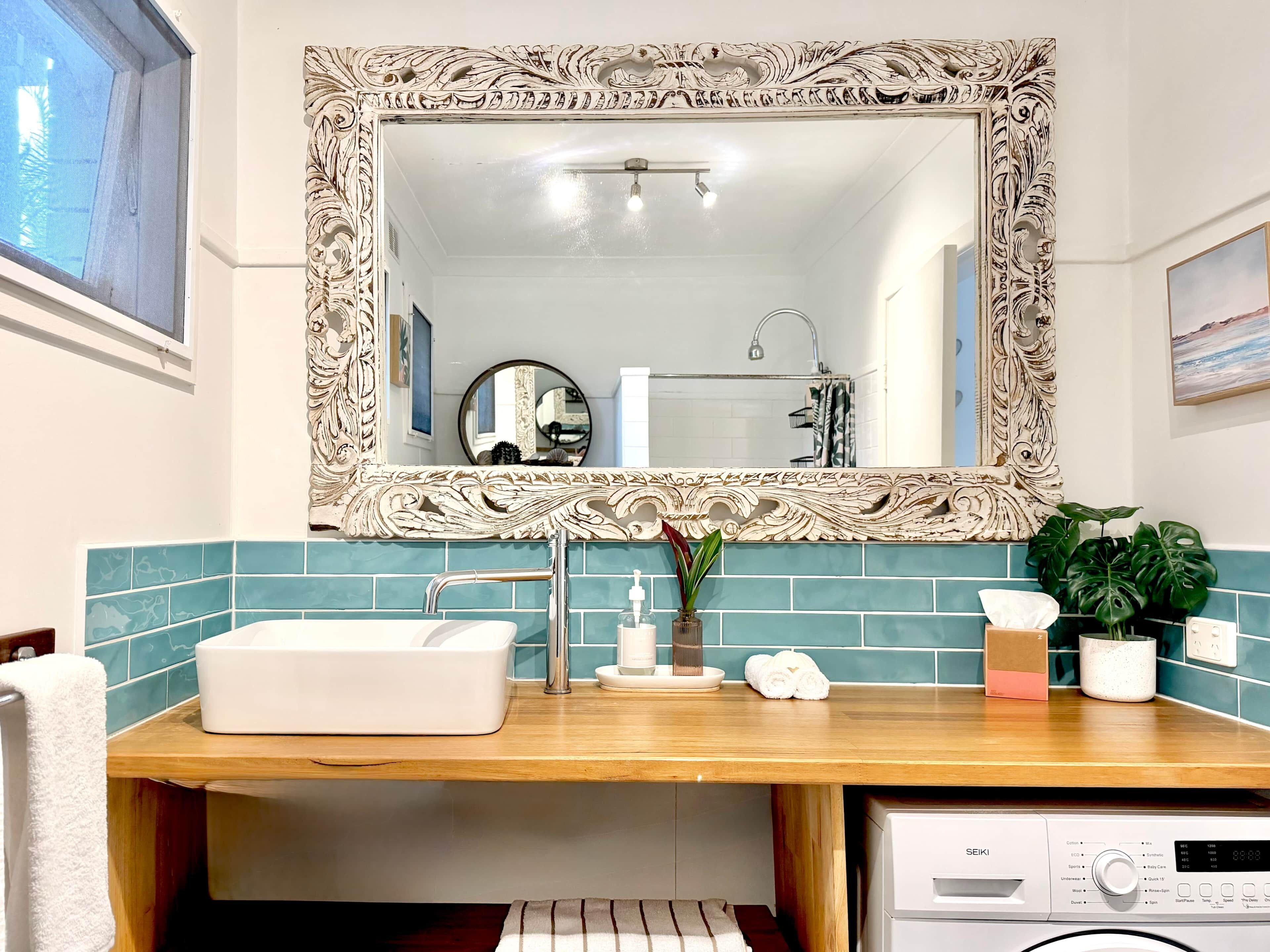 Un baño con un lavabo blanco, un espejo con marco decorativo, una encimera de madera y una lavadora Seiki.