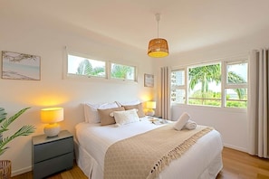 A bedroom with a bed, bedside lamps, a nightstand, a hanging light, and a window with a view of greenery. - Salt - Relaxed Coastal Vibes, Bay Views, Dog Friendly 🐾 (East Ballina)
