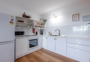 A modern kitchen with white cabinets, a microwave, an oven, a sink, and a countertop with various items. - Salt - Relaxed Coastal Vibes, Bay Views, Dog Friendly 🐾 (East Ballina)