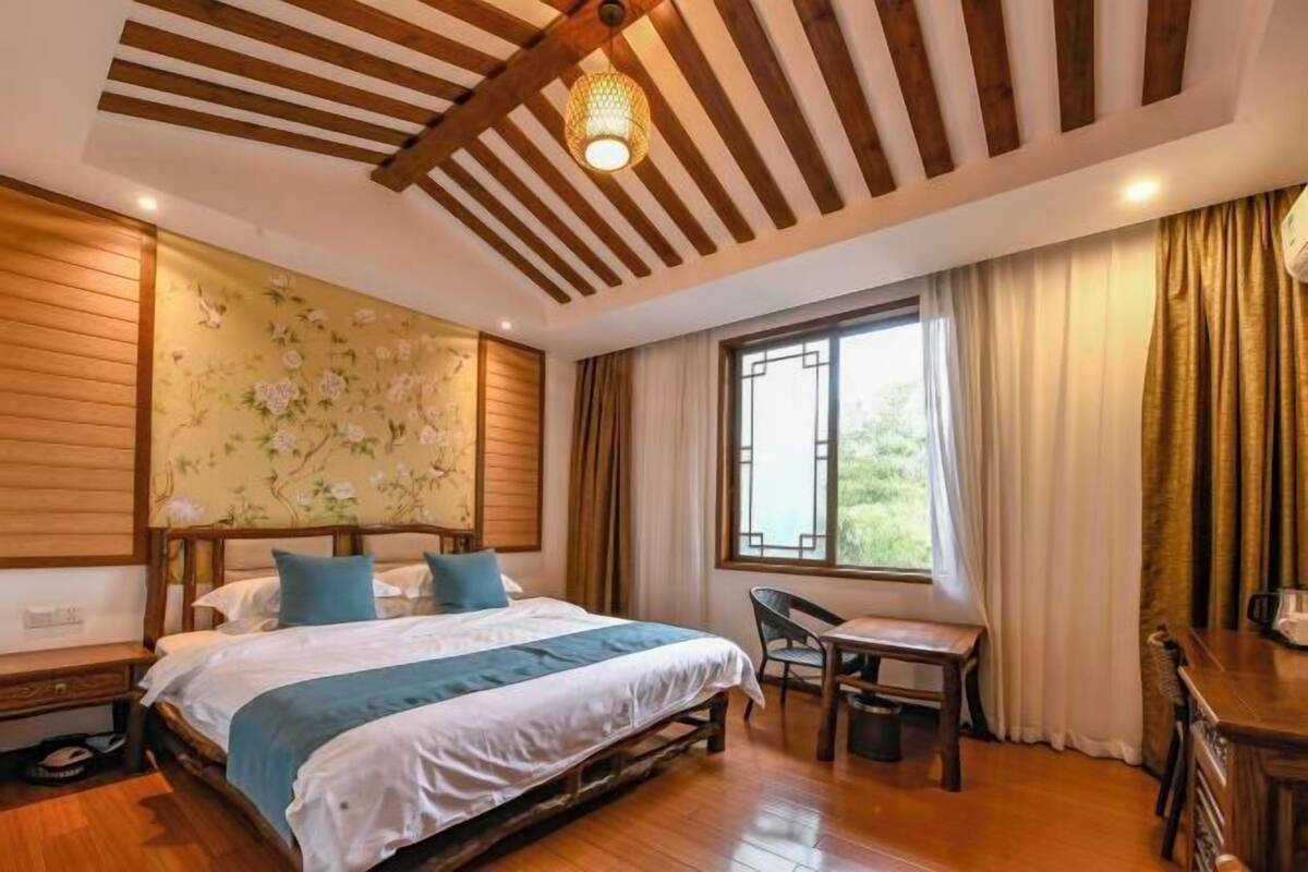 Un dormitorio con cama, escritorio, silla, ventana con cortinas y techo de madera.