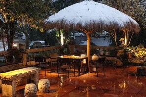 An outdoor dining area with a thatched umbrella, stone seating, and a paved floor. - Zhoujia Shanfang Family Hostel (Wuyishan)