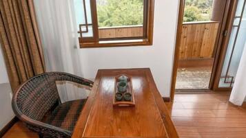 A wooden table with a tray of cups, a wicker chair, and a view of a wooden deck through a window.