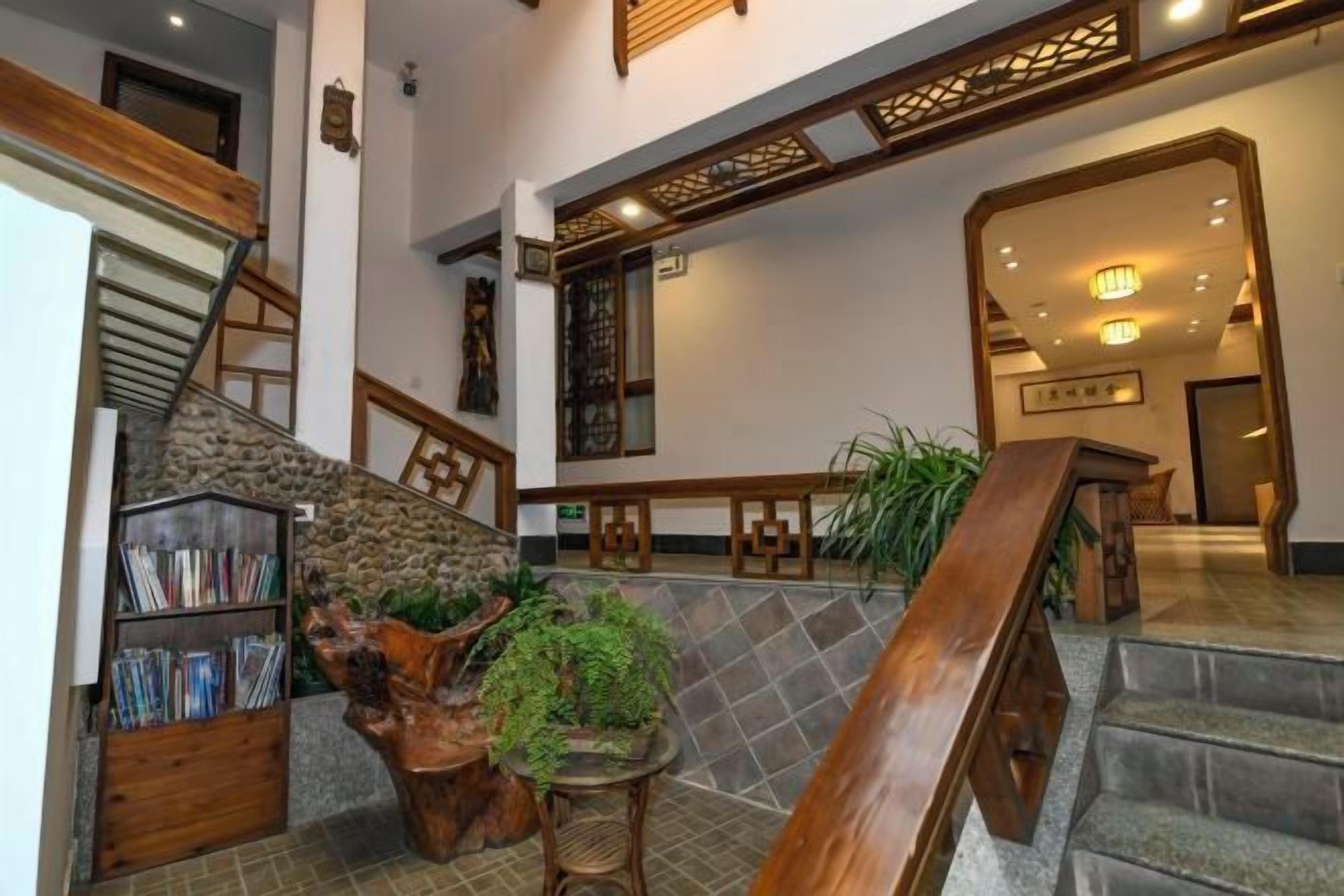 A lobby with a staircase, wooden furniture, a bookshelf, and a potted plant.