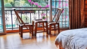 A room with a bed, two wooden chairs, a small table, and a balcony with a wrought iron railing and flowers. - Laozheng Homestay (Yangshuo)