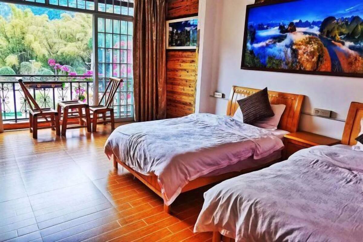 Quarto de hotel com duas camas, uma varanda com cadeiras e um quadro na parede.