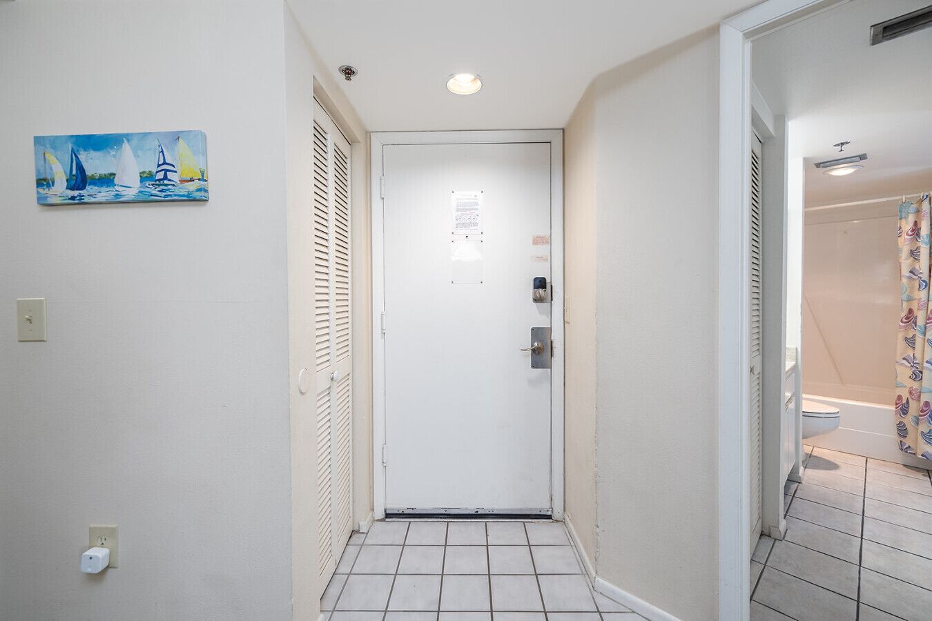 A narrow hallway with a white door, a painting of sailboats on the wall, and a bathroom visible to the right.