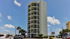 A multi-story hotel with a central courtyard, featuring balconies on each floor and a parking area in front.