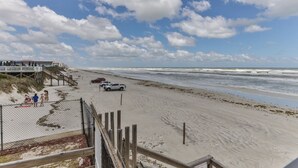A beach view with a wooden pier, a fenced area, and a few people.