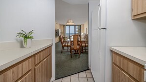 A narrow hallway leading to a dining area with wooden cabinets and a potted plant.