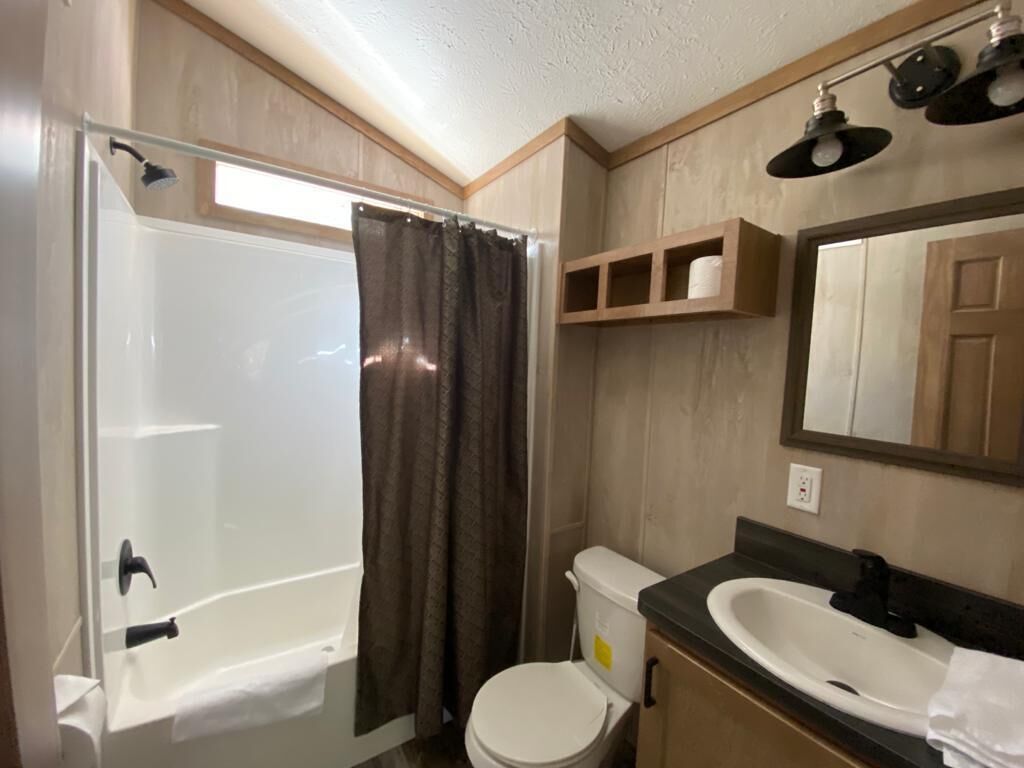 A bathroom with a shower, toilet, sink, and mirror.