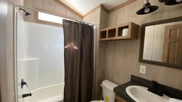 A bathroom with a shower, toilet, sink, and mirror.