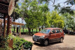 A red car parked in a covered outdoor area with potted plants and a pergola. - Yunshui Hulin Inn Puzhehei (Qiubei)
