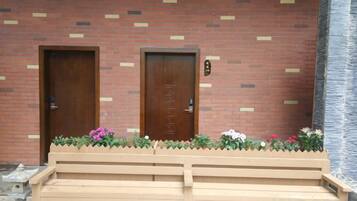A building with two wooden doors, a bench, and a flower bed with pink flowers.