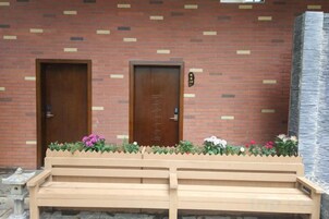 Un edificio con dos puertas de madera, un banco y un parterre con flores rosas.