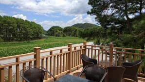 Une terrasse dotée de chaises et d’une table en osier, offrant une vue sur une rizière et des collines boisées.