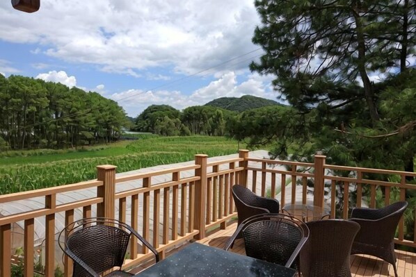 A deck with wicker chairs and a table, overlooking a rice field and forested hills. - Yunshui Hulin Inn Puzhehei (Qiubei)