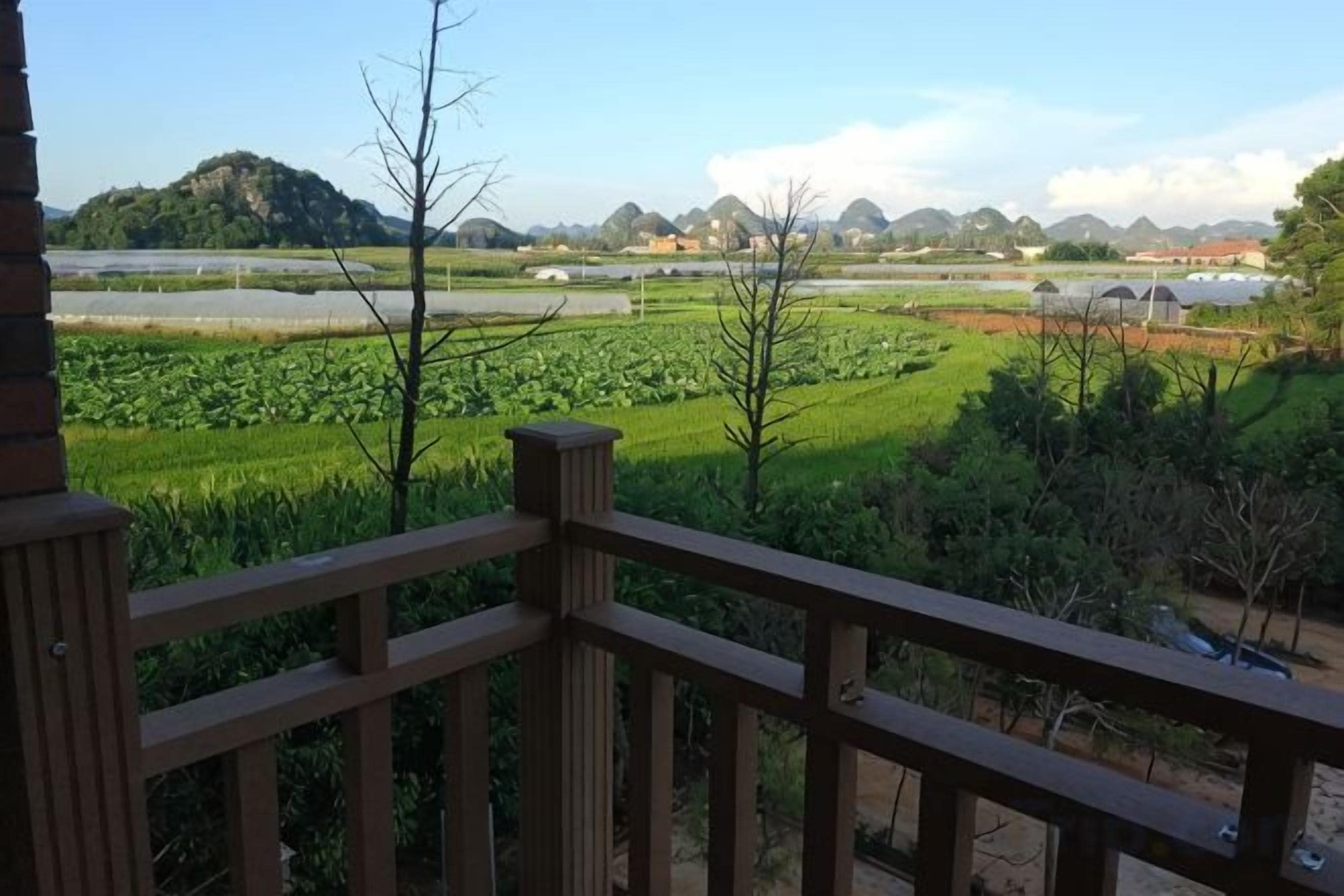 A view from a balcony with a wooden railing, overlooking a green field and distant hills.
