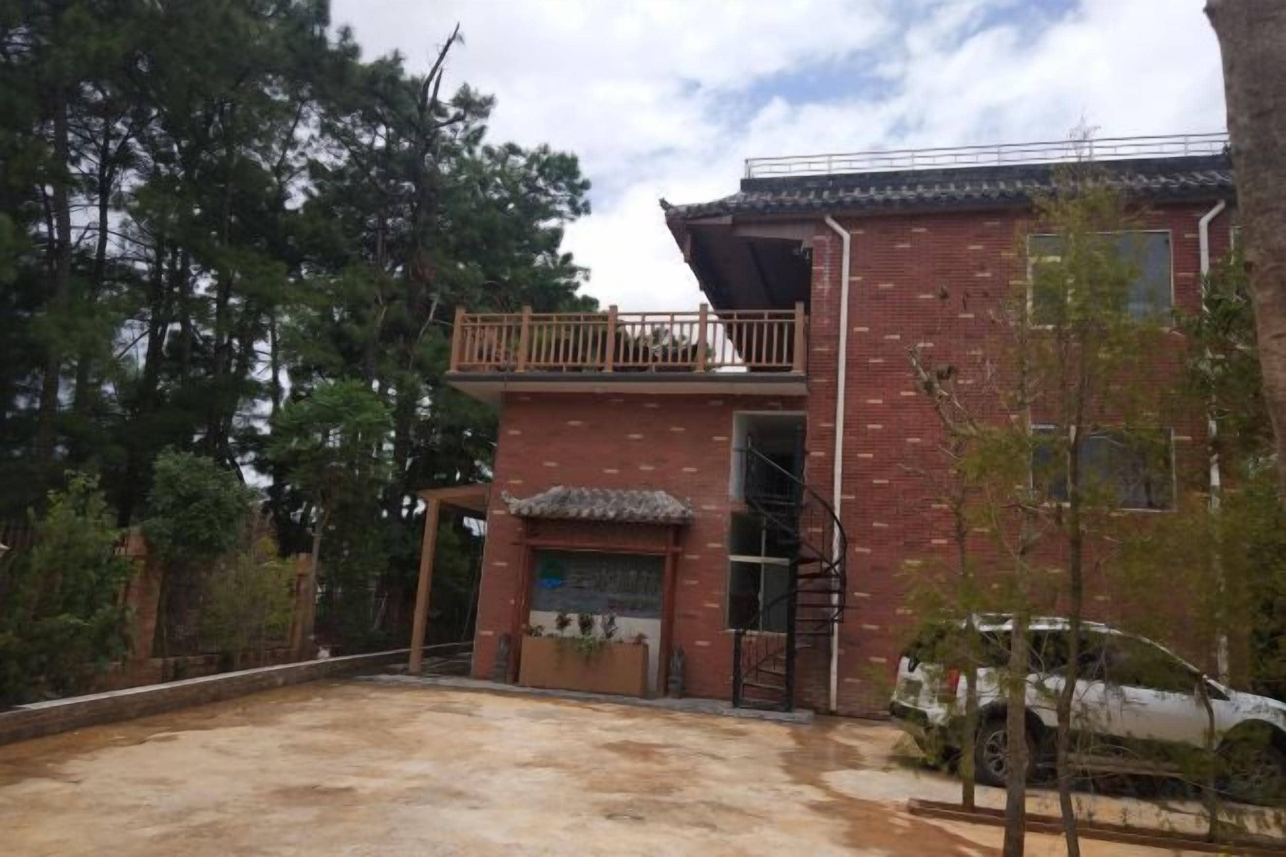 Un edificio de dos pisos con balcón, una escalera y un vehículo estacionado adelante.