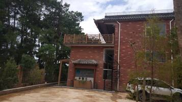 Un edificio de dos pisos con balcón, una escalera y un vehículo estacionado adelante.