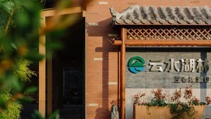 L’entrée d’un bâtiment, avec un toit traditionnel recouvert de tuiles, une porte en bois et une enseigne portant un logo et des caractères chinois.