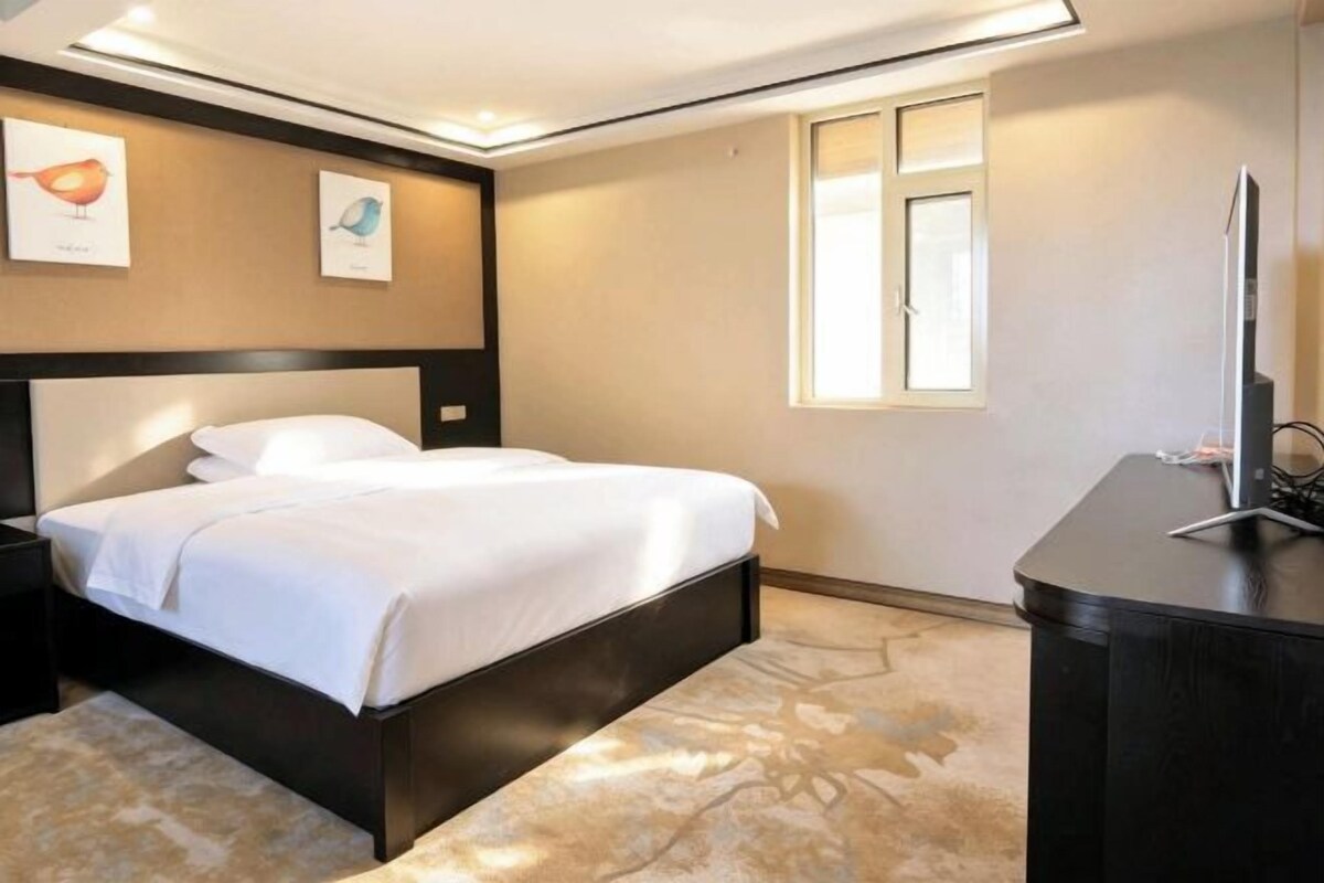A hotel room with a bed, bedside table, and a desk with a computer.