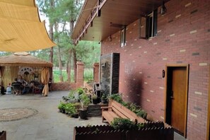A brick building with a wooden door, a covered outdoor seating area, and potted plants. - Yunshui Hulin Inn Puzhehei (Qiubei)