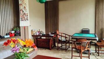 Una habitación con sofá, una mesa con un jarrón de flores, un escritorio con una silla y una mesa de billar.