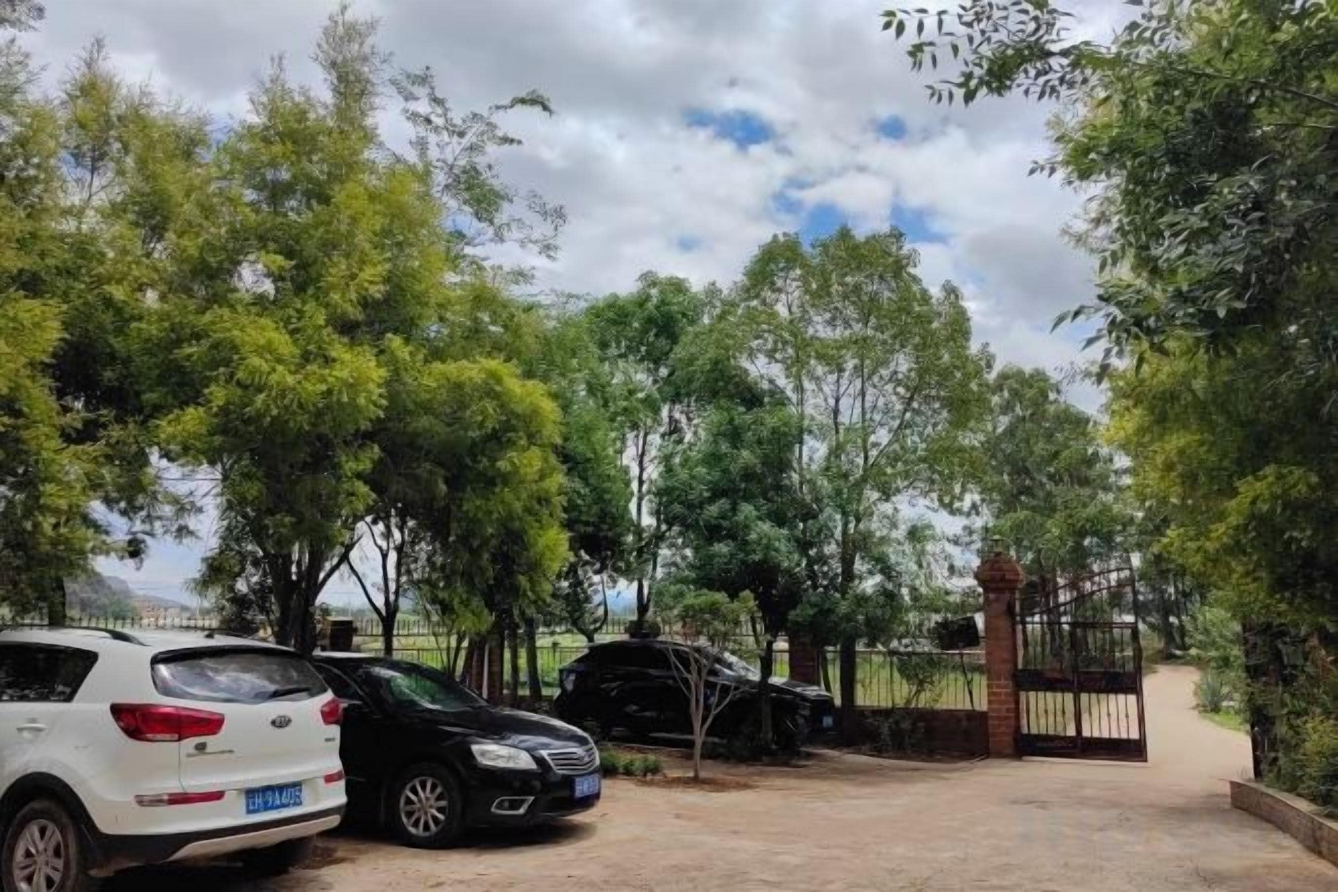 Un estacionamiento con dos coches, árboles y una entrada porticada.