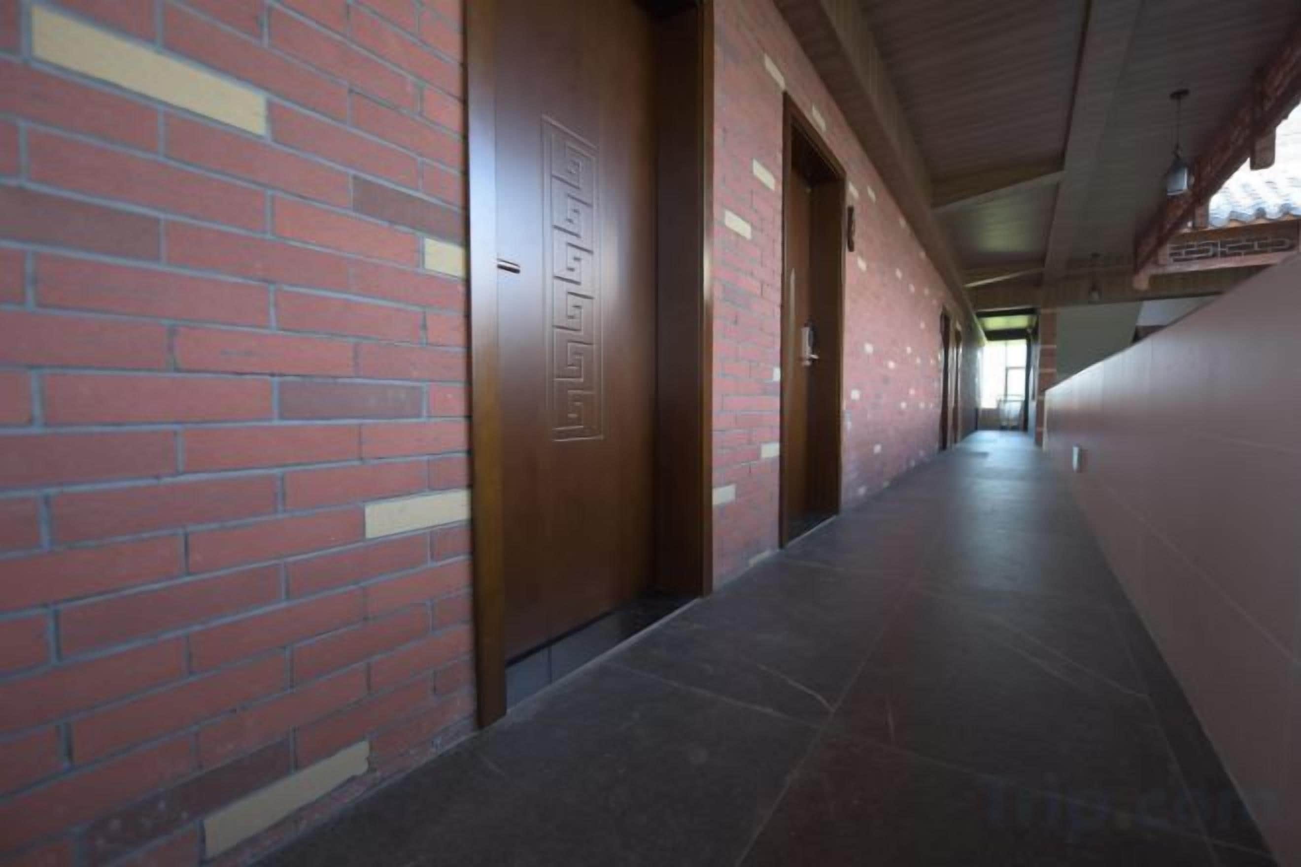 Un couloir aux murs de briques et aux portes en bois, qui mène à une pièce dotée d’une fenêtre.