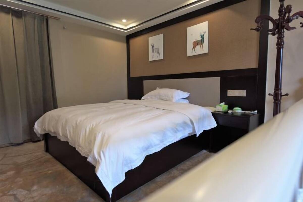 A hotel room with a large bed, a nightstand, a wall-mounted artwork, and a dark-colored headboard.