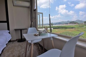 A hotel room with a bed, a small table with a bowl of stones, a chair, and a view of a green landscape through a window. - Yunshui Hulin Inn Puzhehei (Qiubei)
