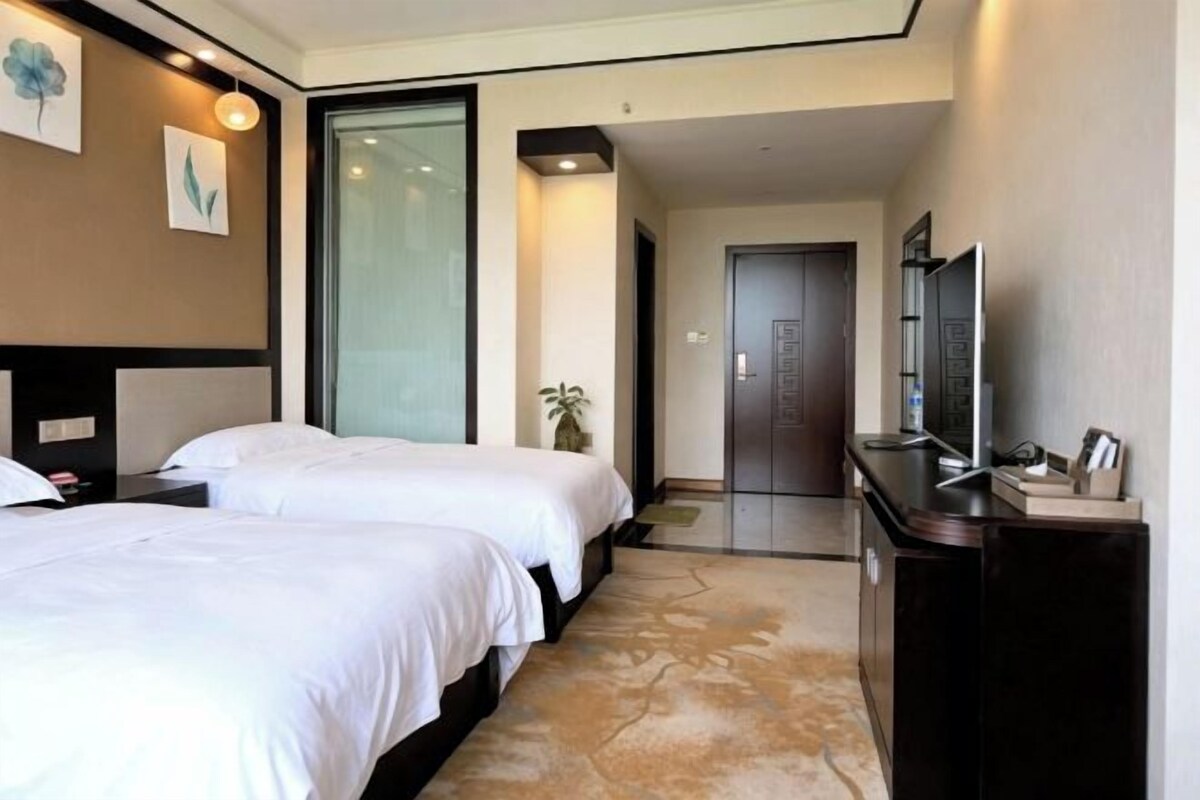 A hotel room with two beds, a desk, a television, and a door leading to another room.
