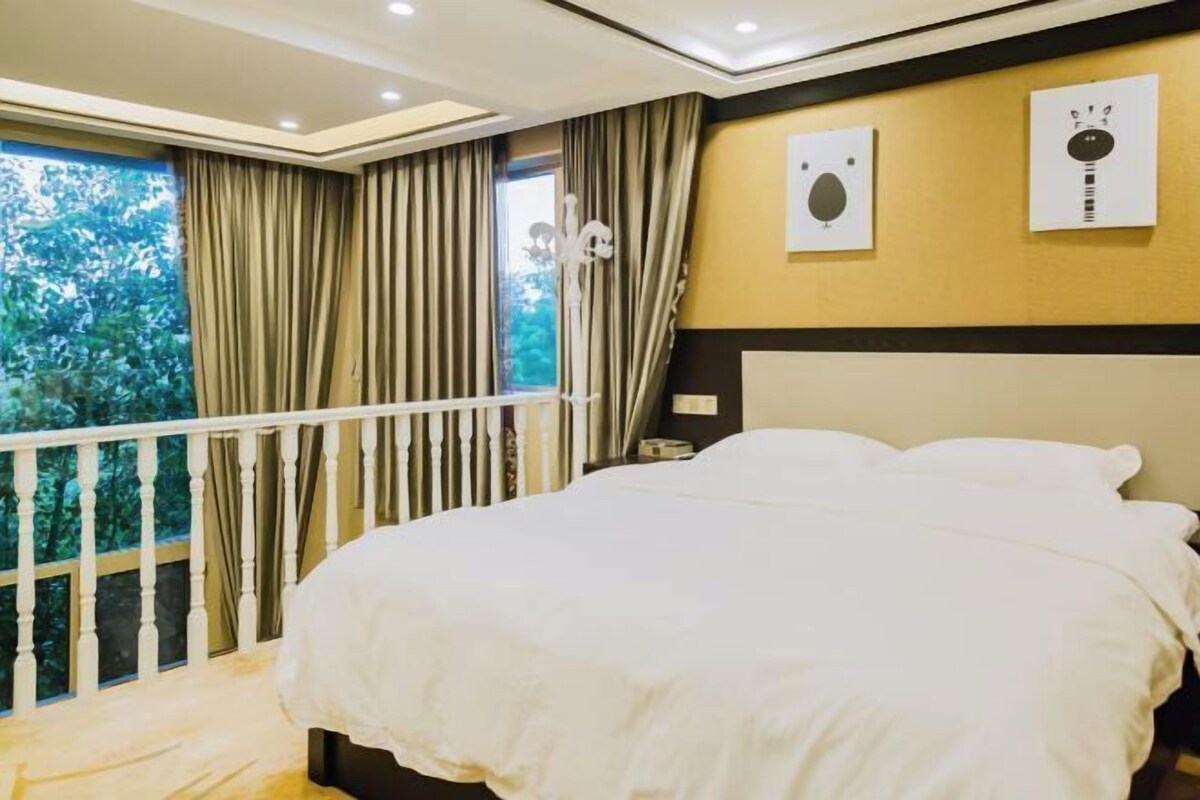 A bedroom with a bed, curtains, a window with a view, and wall art.