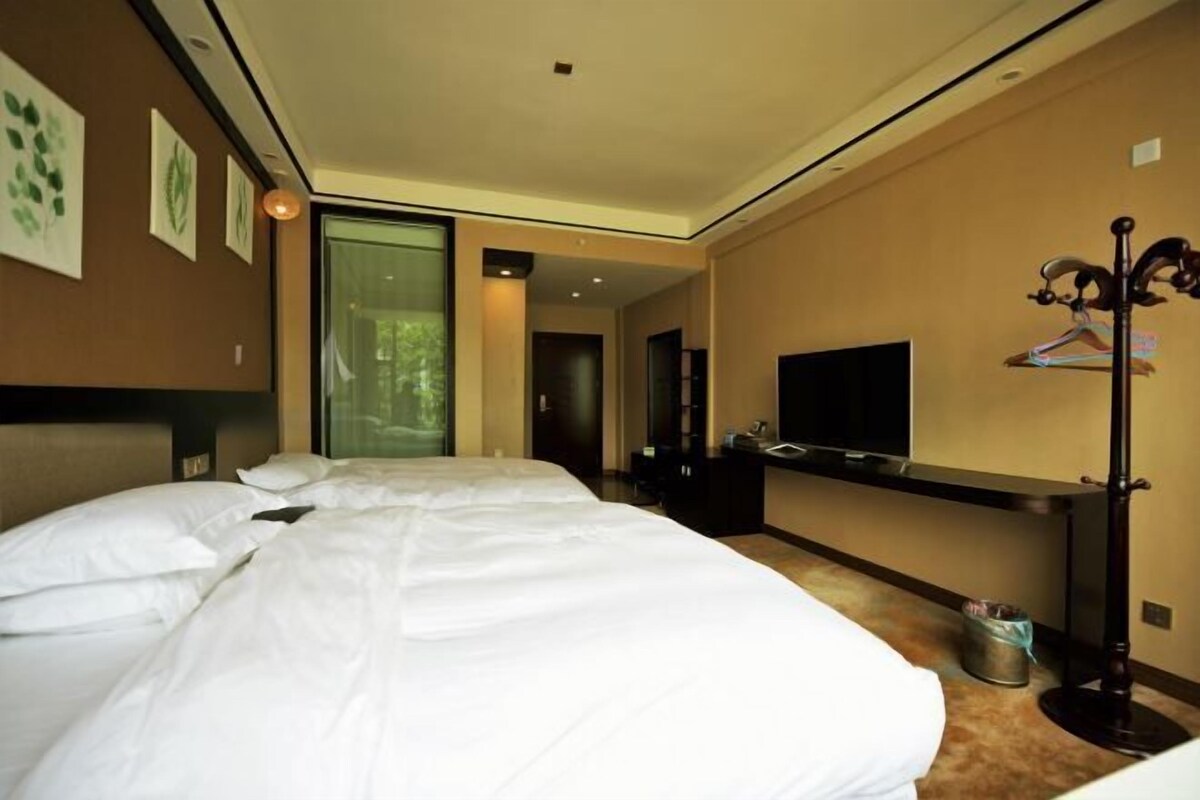 A hotel room with a large bed, a TV, a coat rack, and a hallway leading to another room.