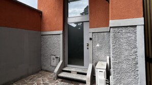 A building entrance with a stone-paved area, a metal door with a glass panel, and a small step leading up to the door. - [ISOLA] Loft Taramelli (Milano)