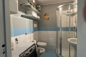 Et badeværelse med toilet, vask, brusebad og håndklædestang.