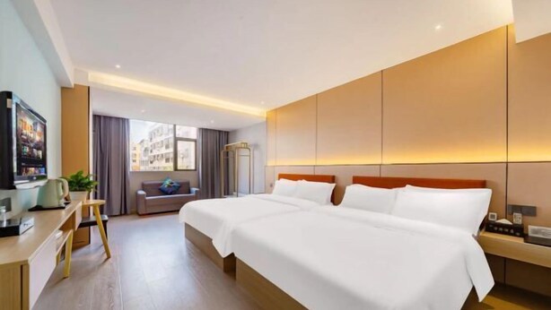 A hotel room with a large bed, a desk, a chair, a TV, and a window with a view of buildings. - Wanlonghote (Cenxi)