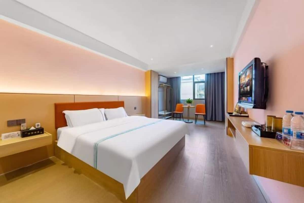 A hotel room with a large bed, a desk with a computer, a TV, and a window with curtains.