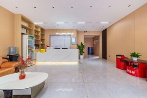 Zona de recepción de hotel con mostrador de recepción, área de espera con sofá y mesa de centro, y mostrador de recepción con diseño rojo.