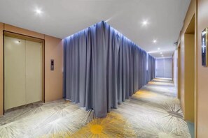 A hotel corridor with a patterned carpet, a blue curtain, and a door on the left. - Wanlonghote (Cenxi)