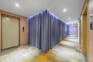 Un pasillo de hotel con alfombra estampada, una cortina azul y una puerta a la izquierda.
