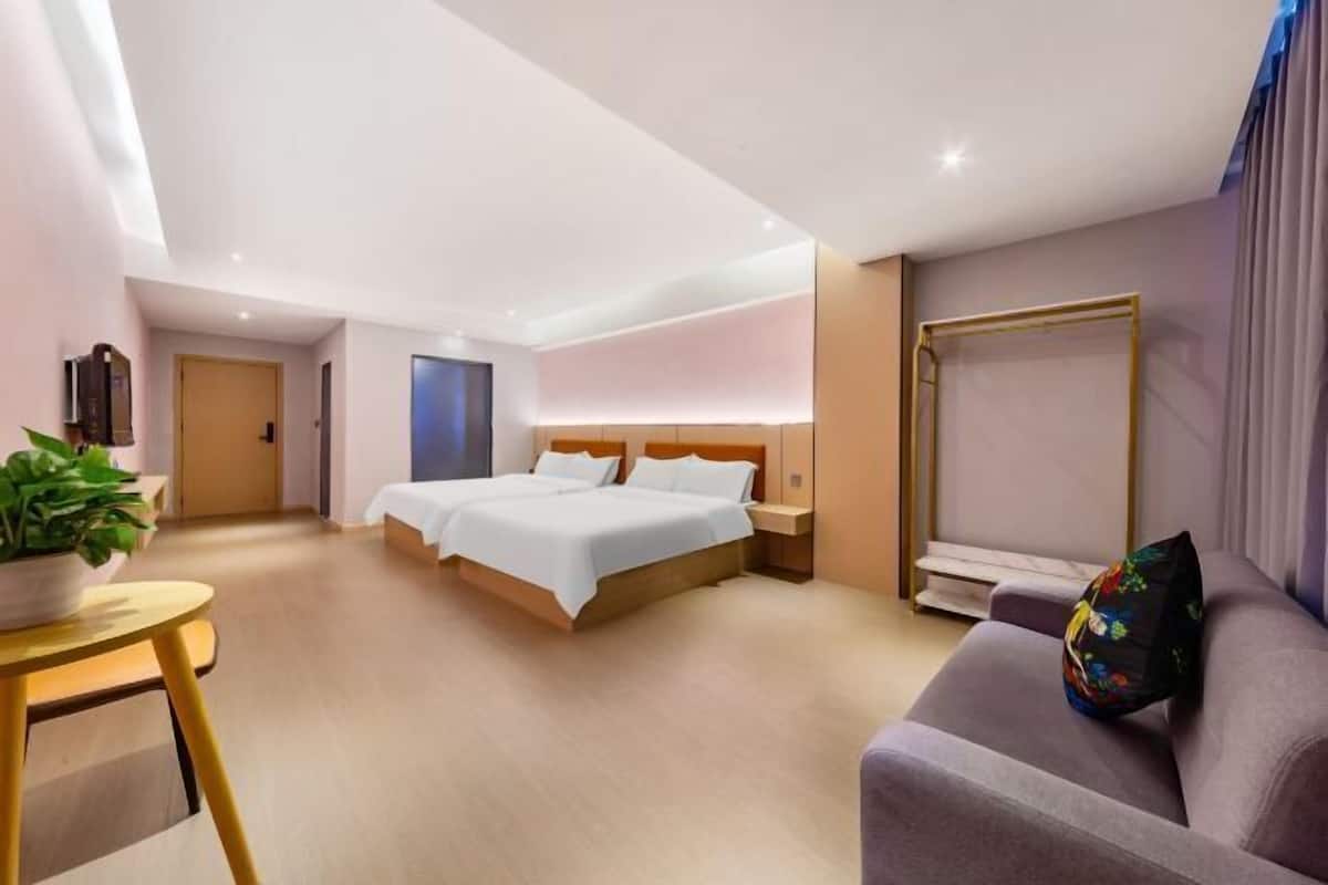 A modern hotel room with a large bed, a sofa, a small table with a plant, and a large window with curtains.