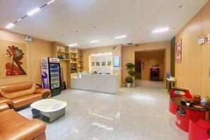A hotel lobby with a reception desk, sofas, a refrigerator, and a coffee machine.