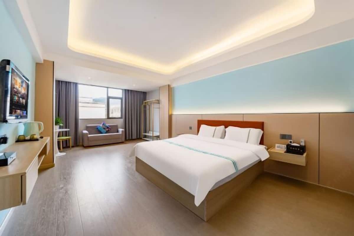 A modern hotel room with a large bed, a desk, a sofa, and a TV.