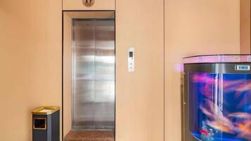 Un ascensor con pantalla digital, un cesto de basura y un acuario con un colorido paisaje acuático.