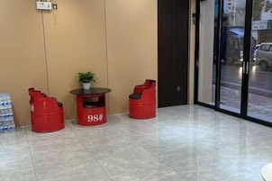 Un hall de hotel con zona de estar, sillones rojos y una mesita con una planta.